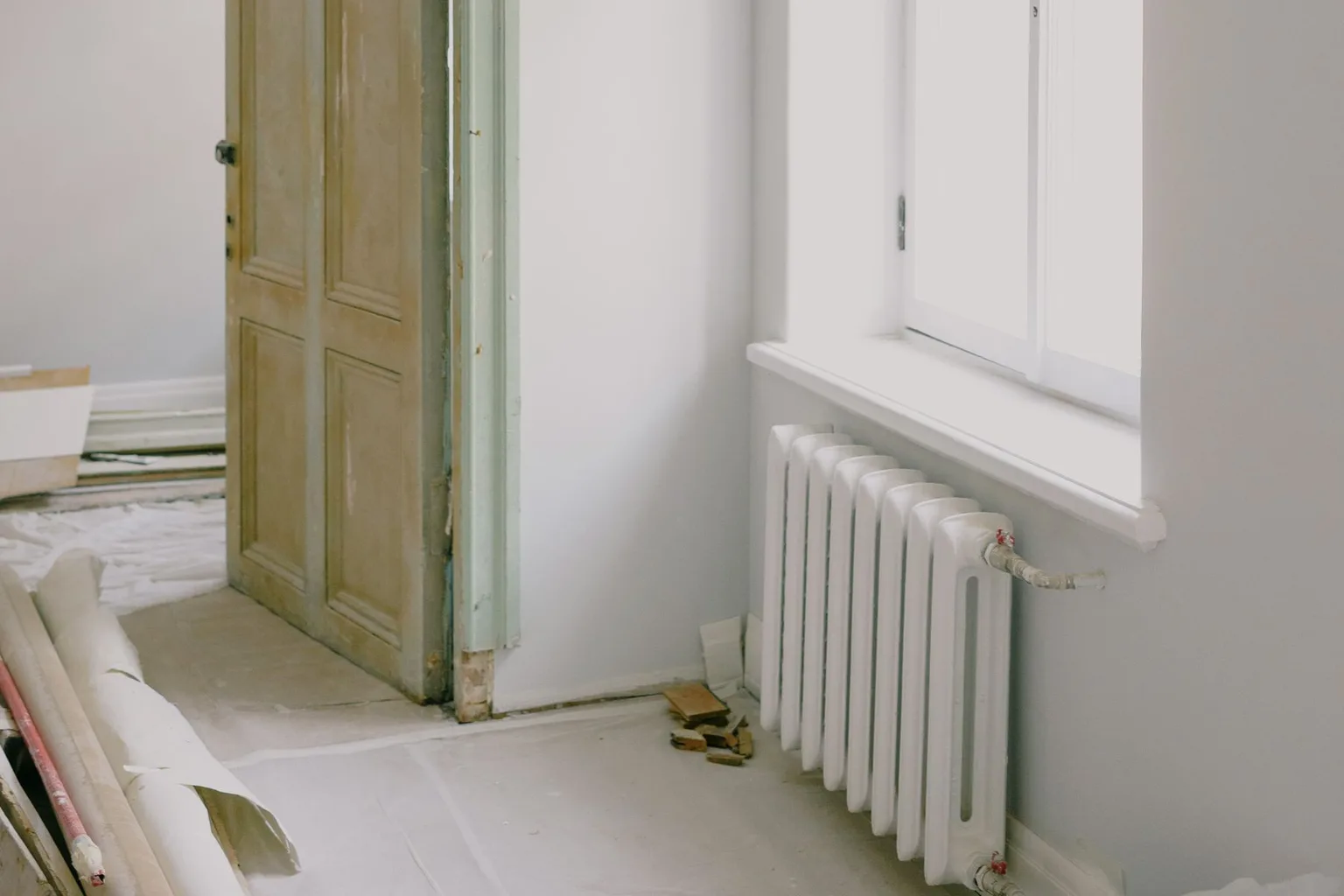 Pièce en rénovation avec porte conservée, radiateur et matériaux au sol